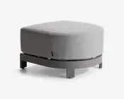 En moderne, rund puf med en lys grå stofpude og en solid, buet base i en matchende neutral farve. Puden har et glat, sømløst udseende med diskrete syninger langs kanterne, og basen har fire korte ben for stabilitet. Det samlede design er minimalistisk og moderne, velegnet til forskellige indretninger.