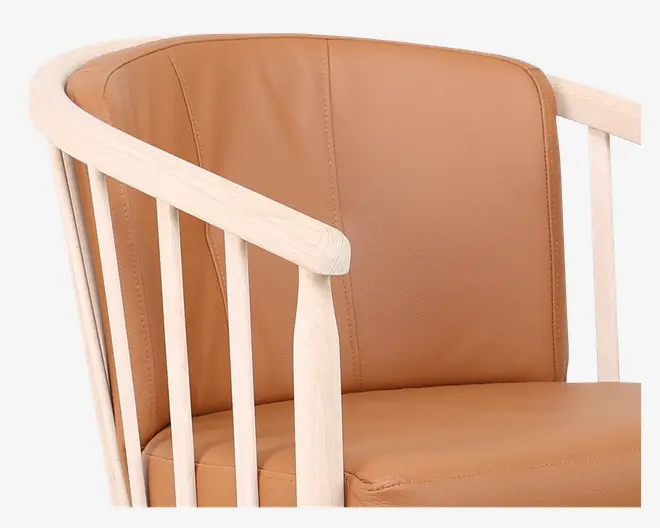 Nærbillede af en stol med stel i lyst træ og lodrette tremmer, der danner ryglæn og armlæn. Sædet og ryglænet er betrukket med glat, lysebrunt læder eller kunstlæder med synlige syninger som detalje. Designet kombinerer moderne og skandinaviske elementer og giver både komfort og stil.