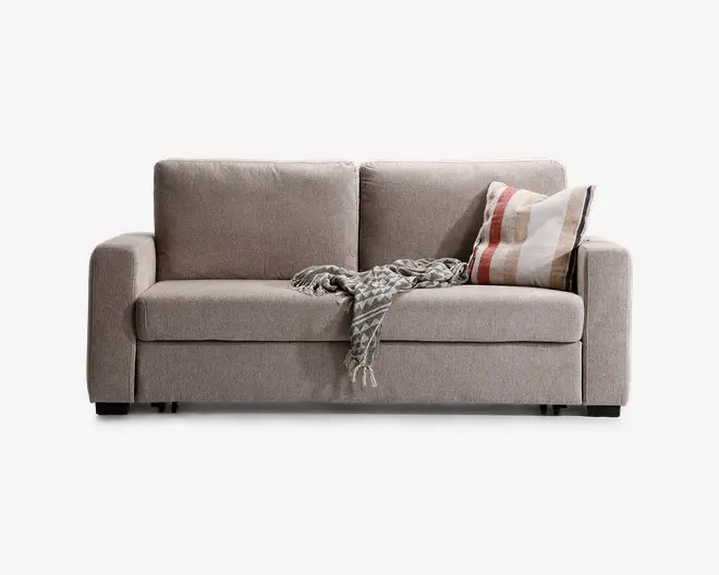 En moderne, lysebeige sofa med rene linjer og rektangulære armlæn. Den har to store, bløde ryghynder og en tyk sædehynde for ekstra komfort. Sofaen er pyntet med en stribet pude i nuancer af brun, rød og creme samt et tekstureret gråt tæppe, der er lagt over sædet. Betrækket ser ud til at være af blødt, vævet stof, og sofaen står på korte, mørke ben.