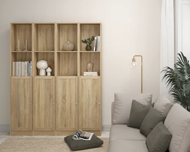 Høj reol i lyst træ med naturlig træstruktur, opdelt i fire lodrette sektioner. Hver sektion har en åben hylde øverst og et lukket skab med låge nederst. De åbne hylder viser dekorative genstande som bøger, vaser, en lille plante og pyntegenstande. Skabslågerne har små runde greb for nem åbning. Designet er minimalistisk og moderne, velegnet til stue eller kontor.