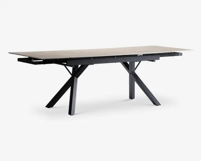 Rektangulært bord med en lys, glat bordplade og sorte, skråtstillede metalben, der er arrangeret i et X-mønster i hver ende. Bordet har et moderne, minimalistisk design med rene linjer og en solid ramme, velegnet til spise- eller arbejdsbrug.