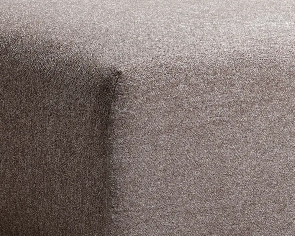Nærbillede af hjørnet på et møbel betrukket med blødt, taupefarvet stof. Stoffet har en glat, fløjlsagtig tekstur og er stramt tilpasset rundt om kanterne, hvilket giver et rent og moderne udtryk.