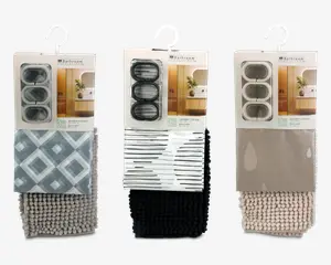 Tre indpakkede badesæt, hver med et badeforhæng, bademåtte og gardinringe. Det første sæt har et geometrisk diamantmønster i grå nuancer med en matchende lysegrå tekstureret måtte. Det andet sæt har et moderne sort-hvidt stribet forhæng med en ensfarvet sort tekstureret måtte. Det tredje sæt viser et taupefarvet forhæng med diskrete vanddråbe-designs og en beige tekstureret måtte. Hvert sæt indeholder tre gardinringe i matchende farver.