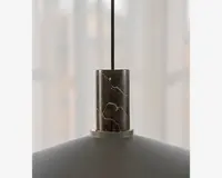 Nærbillede af den øverste del af en pendellampe, der har en cylindrisk marmordetalje med naturlige hvide årer. Marmorelementet forbinder den sorte ophængssnor med den matte lampeskærm nedenunder, hvilket giver lampen et moderne og elegant udtryk.