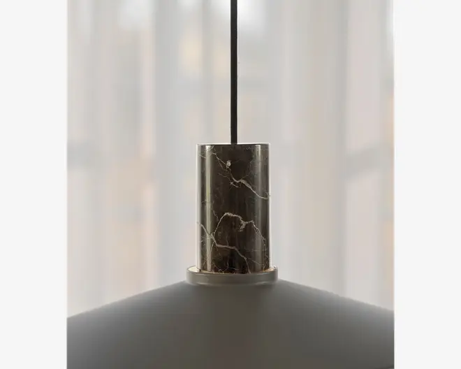 Nærbillede af den øverste del af en pendellampe, der har en cylindrisk marmordetalje med naturlige hvide årer. Marmorelementet forbinder den sorte ophængssnor med den matte lampeskærm nedenunder, hvilket giver lampen et moderne og elegant udtryk.
