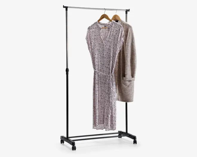 Et fritstående tøjstativ i metal med blank kromfinish. Stativet har en vandret bøjlestang understøttet af to lodrette stolper og står på en base med fire hjul, så det er nemt at flytte. Der hænger to stykker tøj på træbøjler: en lysefarvet, langærmet kjole med diskret blomstermønster og en beige, langærmet cardigan med store forlommer. Stativet har et enkelt, minimalistisk design, der egner sig til organisering eller fremvisning af tøj.