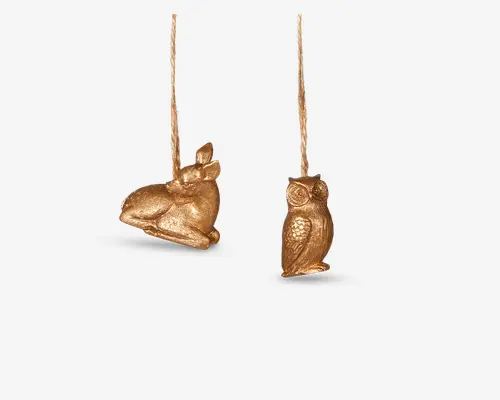 Sæt med to ophængsornamenter i guldfarve, den ene formet som en siddende kanin og den anden som en ugle. Begge har en metallisk overflade med detaljerede teksturer, der fremhæver dyrenes pels og fjer. Hver ornament har et bånd til ophængning.