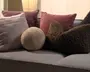 En grå sofa stylet med flere pyntepuder: en stor lysegrå blød pude, en mønstret mauve pude, en støvet rosa rektangulær pude, en lille rund beige pude samt to mørkebrune teksturerede puder med et kruset, bouclé-lignende udtryk.