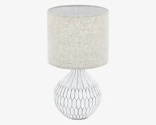 Bordlampe med en rund, kugleformet keramisk fod i hvid med et geometrisk, bikube-lignende sort linjemønster. Lampen har en cylindrisk lampeskærm i beige tekstil med struktur, som giver et blødt og diffust lys. Det samlede design er moderne og neutralt, hvilket passer til mange forskellige indretninger.