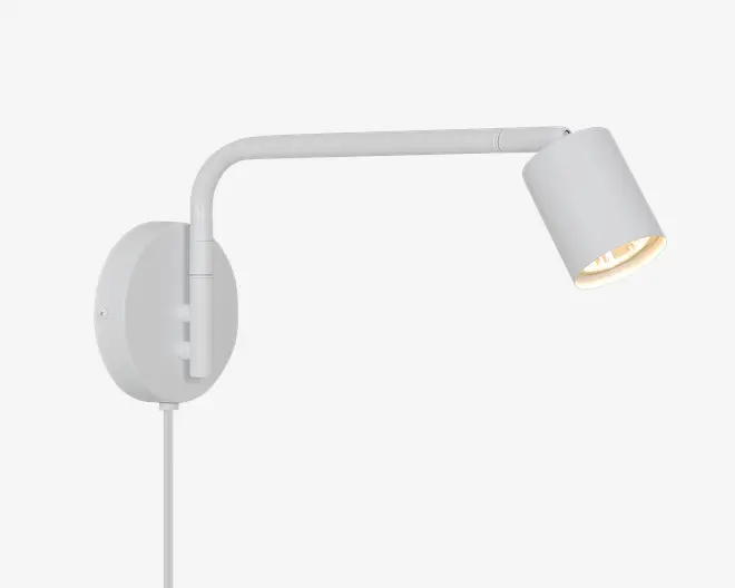 Hvid vægmonteret spotlampe med rund bagplade, buet arm og justerbart cylindrisk lampehoved vinklet nedad.