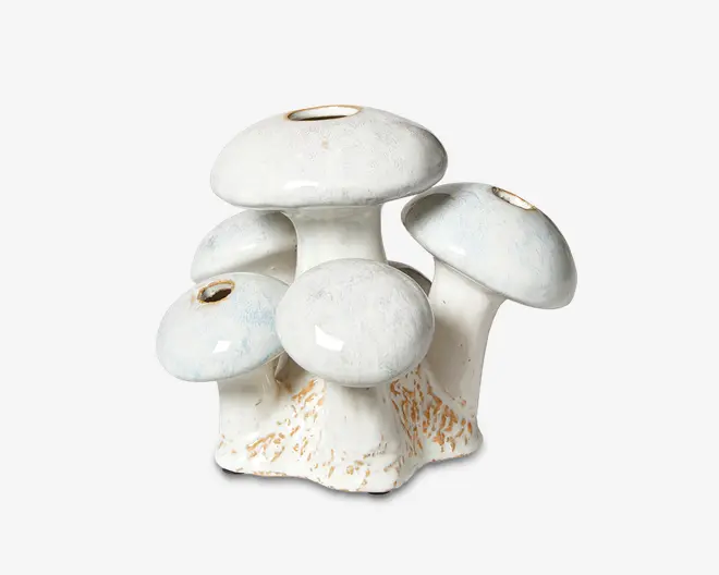 Keramisk vase formet som en klynge af fem svampe, hver med en rund hat og en lille åbning i toppen til blomster. Overfladen er blank hvid med diskrete blå og beige nuancer, og bunden har teksturerede, jordfarvede detaljer, der efterligner naturlige svampestilke.