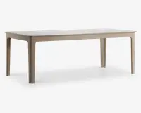 Rektangulært bord med en glat, lys bordplade og matchende ben. Bordet har et minimalistisk design med let afrundede hjørner og kanter, og benene er lige med diskrete indadgående kurver øverst. Overfladen har en mat finish, hvilket giver et moderne og rent udtryk.