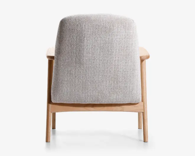 Billedet viser bagsiden af en stol med lyst beige, tekstureret stofbetræk. Stolen har en solid ramme af lyst træ med lige ben og armlæn. Betrækket dækker hele ryglænet og giver et blødt og komfortabelt udtryk, mens trærammen tilføjer et moderne, minimalistisk præg.