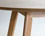 Nærbillede af en lys træbordplade med glat åretegning og skråtstillede ben i træ, hvor samlingen under bordpladen og det enkle, minimalistiske design er synligt.