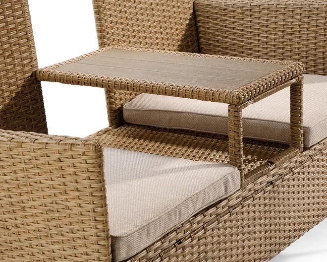 Nærbillede af et udendørs møbel i flet med indbygget, hævet sidebord. Bordet er rektangulært med en ramme i samme flet og en flad overflade med trælook. Siddeområdet har tykke, lyse beige hynder for ekstra komfort. Designet er moderne og funktionelt, hvor bordet er praktisk placeret mellem to siddepladser.