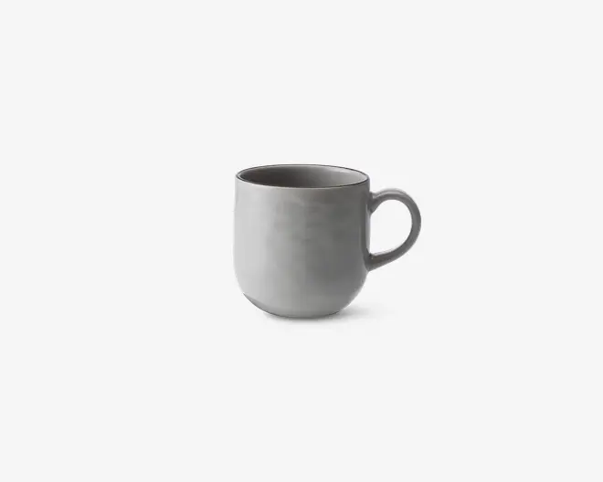 En enkel, moderne kop med en glat, mat lysegrå overflade. Koppen har en rundet form og et stort, behageligt håndtag. Indersiden er også grå og matcher ydersiden. Designet er minimalistisk uden mønstre eller dekorationer.