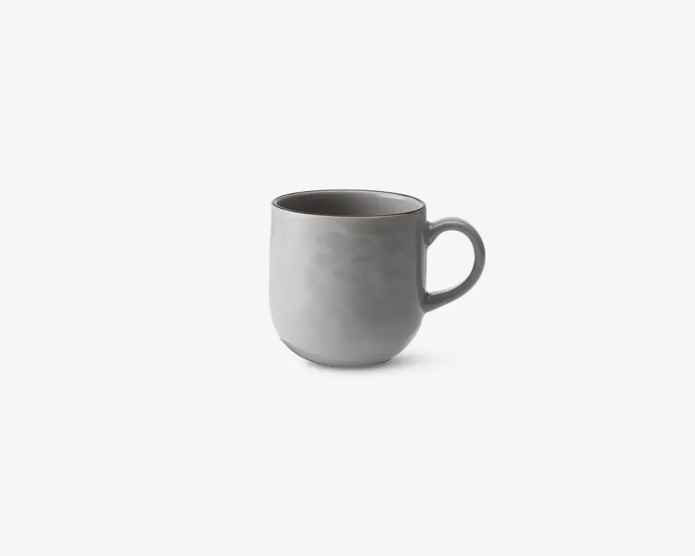 En enkel, moderne kop med en glat, mat lysegrå overflade. Koppen har en rundet form og et stort, behageligt håndtag. Indersiden er også grå og matcher ydersiden. Designet er minimalistisk uden mønstre eller dekorationer.