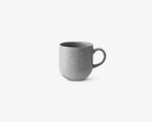 En enkel, moderne kop med en glat, mat lysegrå overflade. Koppen har en rundet form og et stort, behageligt håndtag. Indersiden er også grå og matcher ydersiden. Designet er minimalistisk uden mønstre eller dekorationer.