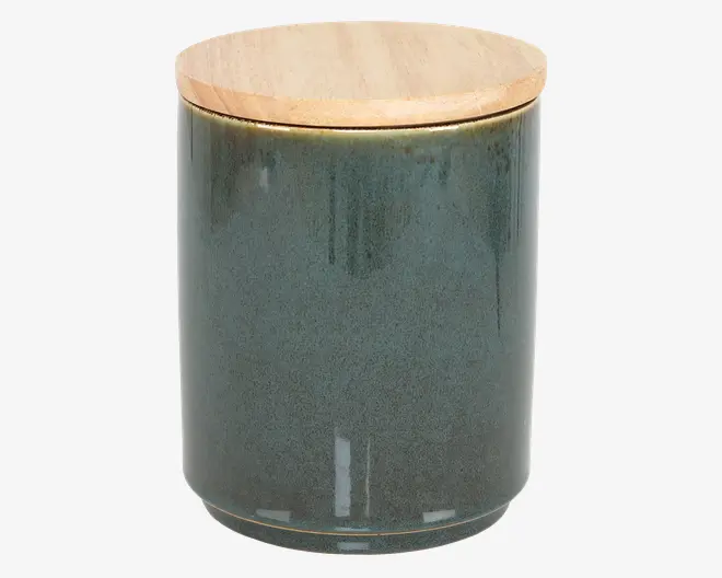 Cylindrisk beholder med en glat, blank mørkegrøn keramisk krop og et fladt, rundt låg af lyst træ. Låget passer tæt på toppen, og keramikken har diskrete farvevariationer og en let plettet overflade.
