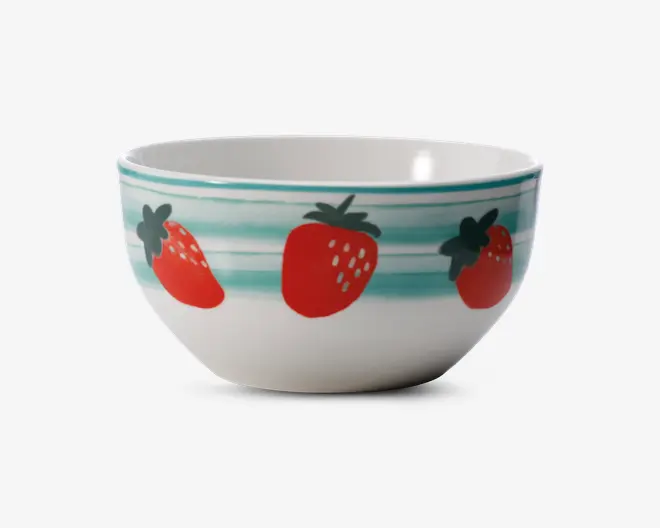 Hvid keramikskål med et legende design af store røde jordbær og grønne blade rundt om ydersiden. Skålen har også vandrette turkisblå striber nær kanten, som giver et farverigt præg. Indersiden er ensfarvet hvid, og skålen har en glat, blank overflade.