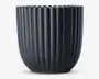 En mat sort beholder med lodrette riller og en afrundet, let tilspidset form. Kanten har en blødt bølget dekoration, som giver et elegant udtryk. Overfladen er glat, og designet er moderne og minimalistisk.