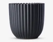 En mat sort beholder med lodrette riller og en afrundet, let tilspidset form. Kanten har en blødt bølget dekoration, som giver et elegant udtryk. Overfladen er glat, og designet er moderne og minimalistisk.