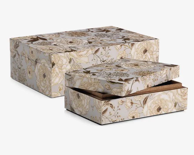 To rektangulære æsker med matchende låg, dekoreret med et elegant blomstermønster i nuancer af creme, beige og guld. Æskerne har en glat, blank overflade, og blomstermotivet viser detaljerede roser og blade. Den ene æske er let åben og afslører en brun indvendig foring. Æskerne kan stables og er velegnede til dekorativ opbevaring eller gaveindpakning.