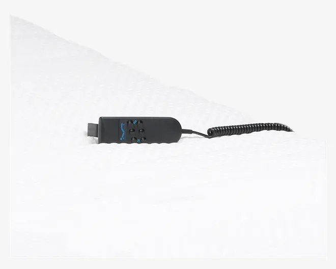 Et nærbillede af en sort fjernbetjening med ledning, der ligger på en hvid, tekstureret overflade. Fjernbetjeningen har flere knapper til justering af indstillinger, herunder op- og ned-pile samt ekstra funktionsknapper, sandsynligvis til at styre hældning og andre funktioner. Den spiralformede ledning er fastgjort til fjernbetjeningen, hvilket giver nem rækkevidde og fleksibilitet.