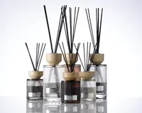 En gruppe elegante glasbeholdere med lodrette rillede strukturer, hver med et lyst trælåg og fyldt med sorte duftpinde. Beholderne varierer i størrelse og farve, herunder klare, røggrå og ravfarvede nuancer. Hver beholder har en metallabel på forsiden, hvilket giver et eksklusivt og sofistikeret udtryk.