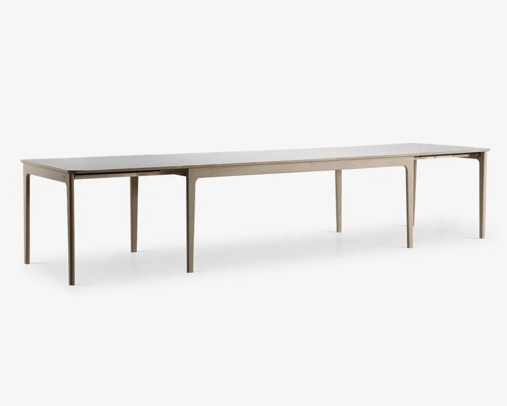 Rektangulært bord med lys træfinish, designet med en lang og udvidet form, der egner sig til mange siddepladser. Bordet har rene, lige linjer og seks slanke ben, hvilket giver det et moderne og minimalistisk udtryk.