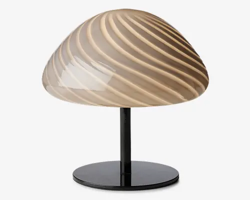 Bordlampe med en kuppelformet glasskærm, der har et beige og brunt swirl-mønster, som giver et blødt og diffust lys. Skærmen hviler på en slank, sort cylindrisk stamme og en rund, flad fod, hvilket giver lampen et moderne og kunstnerisk udtryk.