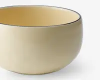 En rund, glat keramikskål med blank cremefarvet overflade både indvendigt og udvendigt. Skålens kant er markeret med en tynd, mørk streg, som giver et diskret dekorativt præg. Skålen har et enkelt, minimalistisk design uden hank eller mønster.