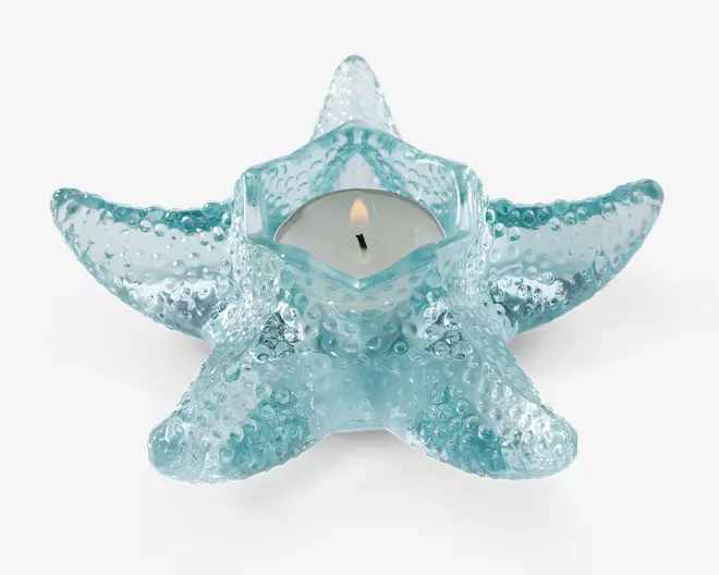 Et fyrfadsstage formet som en søstjerne, lavet af tekstureret, gennemsigtigt blå glas. Stagen har forhøjede knopper, der efterligner en søstjernes naturlige overflade, og en central sekskantet fordybning, der passer til et almindeligt fyrfadslys.