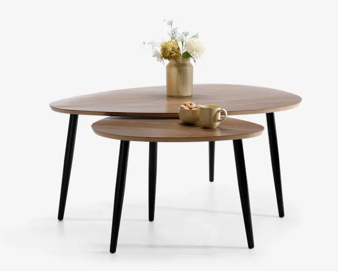 Sæt med to runde indskudsborde med glatte, mellembrune træplader og slanke, sorte koniske ben. Det større bord er pyntet med en rillet beige vase med hvide og gule blomster, mens det mindre bord har et beige krus, en lille skål og et wienerbrød. Bordene kan placeres sammen eller hver for sig for alsidig brug.