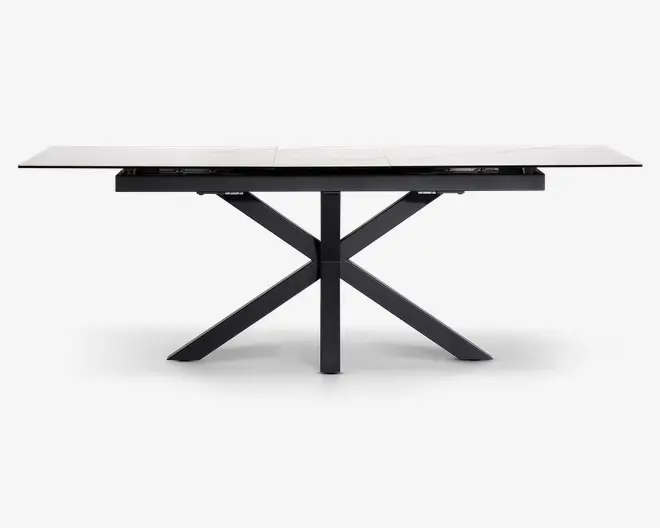 Rektangulært bord med en hvid, marmorlignende bordplade og et moderne sort metalstel. Bordpladen ser ud til at være udtrækkelig med synlige samlinger, der indikerer tillægsplader. Stellet har et geometrisk krydsben-design, som giver stabilitet og et moderne udtryk.