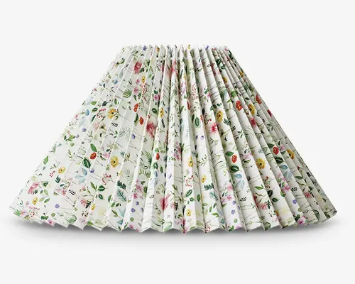 Plisseret lampeskærm med bred, udvidet form. Stoffet har et fint blomstermønster med forskellige farverige blomster og grønne blade på hvid baggrund. Plisseringerne giver et tekstureret, tredimensionelt udtryk, og stilen er let og dekorativ – perfekt til at tilføje et friskt, botanisk præg til rummet.
