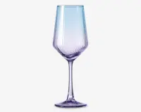 Elegant glas med høj, slank stilk og en facetslebet skål med lodrette riller. Glasset har en diskret farvegradient, der går fra lyseblå i toppen til blød lilla ved bunden. Designet kombinerer moderne æstetik med et strejf af sofistikation, hvilket gør det velegnet til særlige lejligheder.