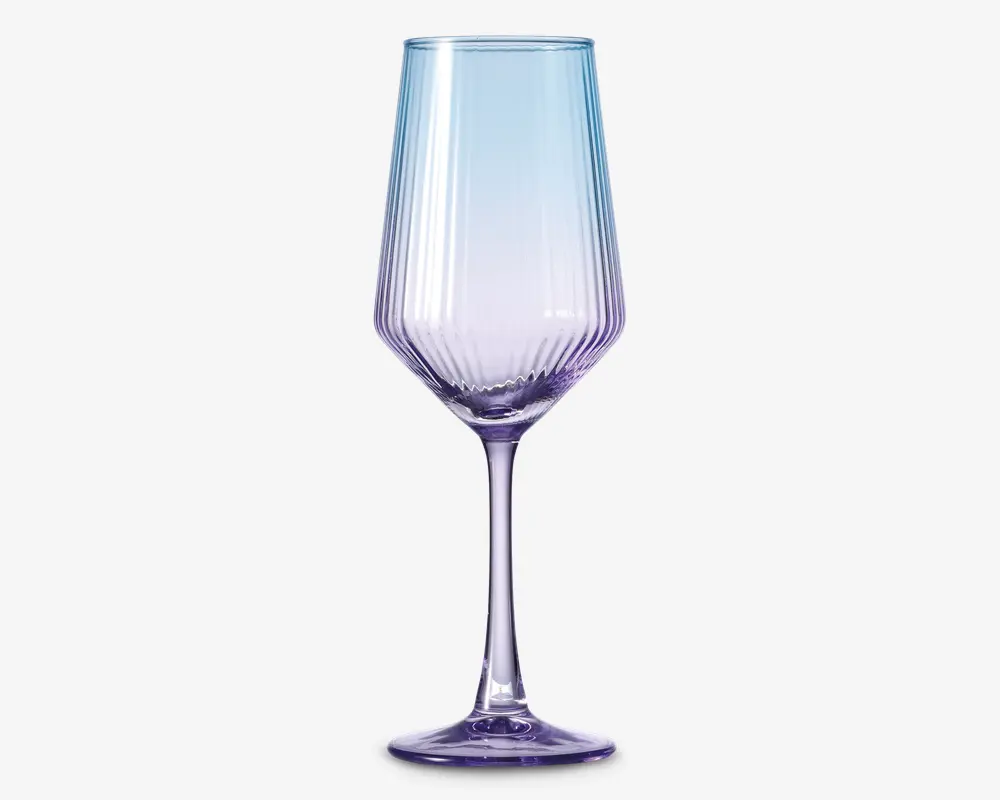 Elegant glas med høj, slank stilk og en facetslebet skål med lodrette riller. Glasset har en diskret farvegradient, der går fra lyseblå i toppen til blød lilla ved bunden. Designet kombinerer moderne æstetik med et strejf af sofistikation, hvilket gør det velegnet til særlige lejligheder.