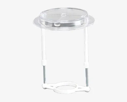 Gennemsigtigt plastiklåg med en central knop, designet til at passe over et rundt serveringsfad. Låget holdes oppe af to lodrette stænger, der er fastgjort til en cirkulær bund, hvilket gør det muligt at løfte og holde låget over fadet. Konstruktionen virker let og nem at samle eller adskille til rengøring og opbevaring.
