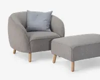 Et moderne lænestol- og fodskammelsæt betrukket med lysegråt stof. Lænestolen har en rundet ryg og sider, en tyk polstret sædehynde og fire lyse træben. Der medfølger en enkelt lyseblå-grå pyntepude for ekstra komfort. Fodskamlen er rektangulær med afrundede kanter og står også på fire lyse træben, som matcher stolens design.