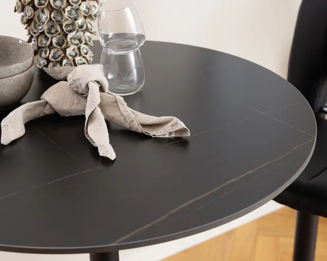 Rund bordplade med mat sort finish og diskrete, tynde årer. Overfladen er glat og moderne med en let glans. Bordkanten er blødt afrundet, og bordet fremstår solidt med et minimalistisk design.