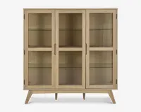 Rektangulært skab med tre glaslåger, lys træramme og skråtstillede ben. Indeholder to indvendige glashylder i hver sektion, hvilket giver god plads til udstilling. Håndtagene er integreret i træet for et stilrent og minimalistisk udtryk.