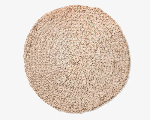 Rund, håndvævet måtte lavet af naturlige, lyse beige fibre. Måtten har et åbent, luftigt hæklemønster med synlige løkker og en let tekstureret overflade. Kanterne er blødt afrundede, og det samlede udtryk er rustikt og håndlavet, hvilket gør den velegnet til at tilføje et naturligt præg til boligindretningen.