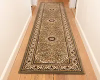 En lang, rektangulær løber med et indviklet blomster- og medaljonmønster i dæmpede jordfarver, herunder olivengrøn, beige og bordeaux. Tæppet har tre cirkulære medaljoner jævnt fordelt langs længden, omgivet af en detaljeret kant med snoede vinmønstre. Kanterne er pænt afsluttet, og tæppet ligger fladt på et lyst trægulv i en gang.