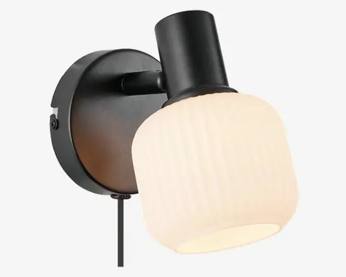 Væghængt lampe med mat sort metalbase og arm samt en cylindrisk, rillet hvid glasskærm. Skærmen spreder lyset blødt og har en diskret lodret struktur. Lampen har et moderne, minimalistisk design og egner sig til retningsbestemt belysning.