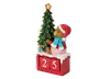 En dekorativ julefigur med en bamse iført rød nissehue, rød frakke og blå tørklæde, der sidder ved siden af et juletræ pyntet med røde kugler og en gylden stjerne i toppen. Bamsen sidder på en rød blok med "sne" på toppen og to hvide talterninger, der viser "25". Små indpakkede gaver ligger under træet og fuldender det festlige udtryk.