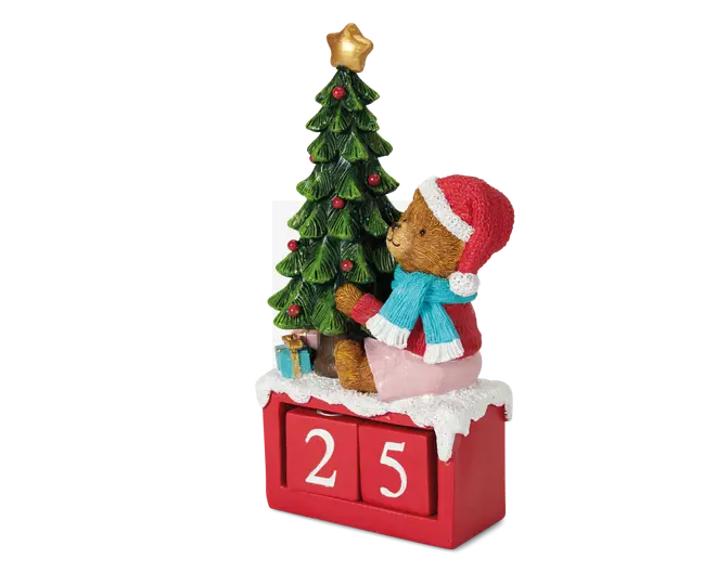 En dekorativ julefigur med en bamse iført rød nissehue, rød frakke og blå tørklæde, der sidder ved siden af et juletræ pyntet med røde kugler og en gylden stjerne i toppen. Bamsen sidder på en rød blok med "sne" på toppen og to hvide talterninger, der viser "25". Små indpakkede gaver ligger under træet og fuldender det festlige udtryk.