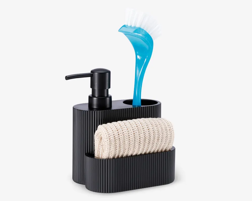 En moderne, sort køkkenorganisator i rillet plast med indbygget sæbepumpe, et rum til en opvaskebørste med blåt håndtag og hvide børster samt en frontlomme med en sammenrullet beige strikket klud. Organisatoren har et stilrent og kompakt design med separate sektioner, der holder rengøringsredskaberne organiseret og let tilgængelige.