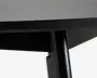 Nærbillede af et sort, cylindrisk metalben under en mørk træoverflade med en skrå underside og en ren, moderne finish.