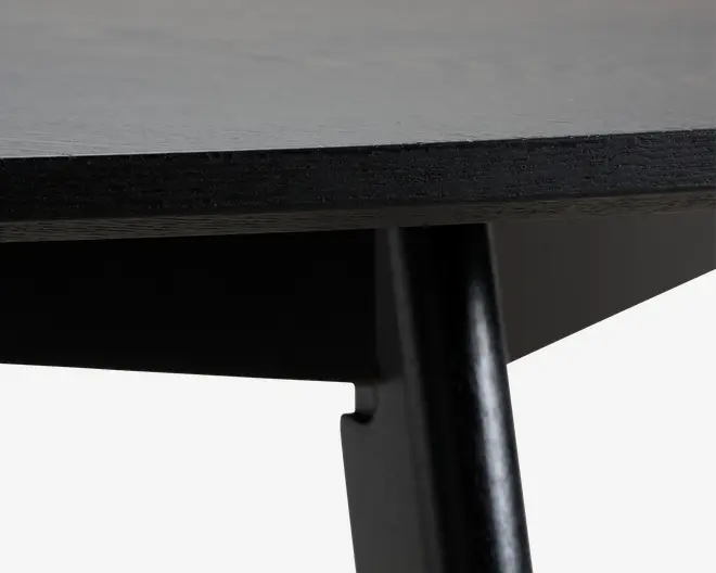 Nærbillede af et sort, cylindrisk metalben under en mørk træoverflade med en skrå underside og en ren, moderne finish.